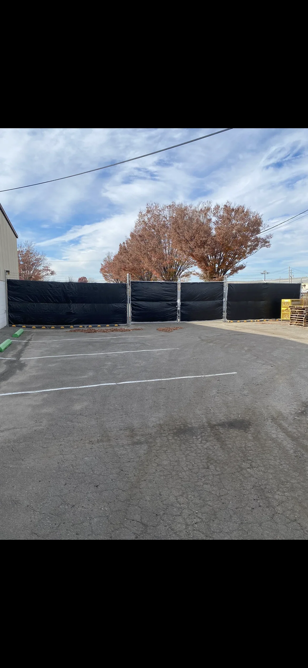 Black privacy fence with wind screen material installed on wooden posts in commercial lot