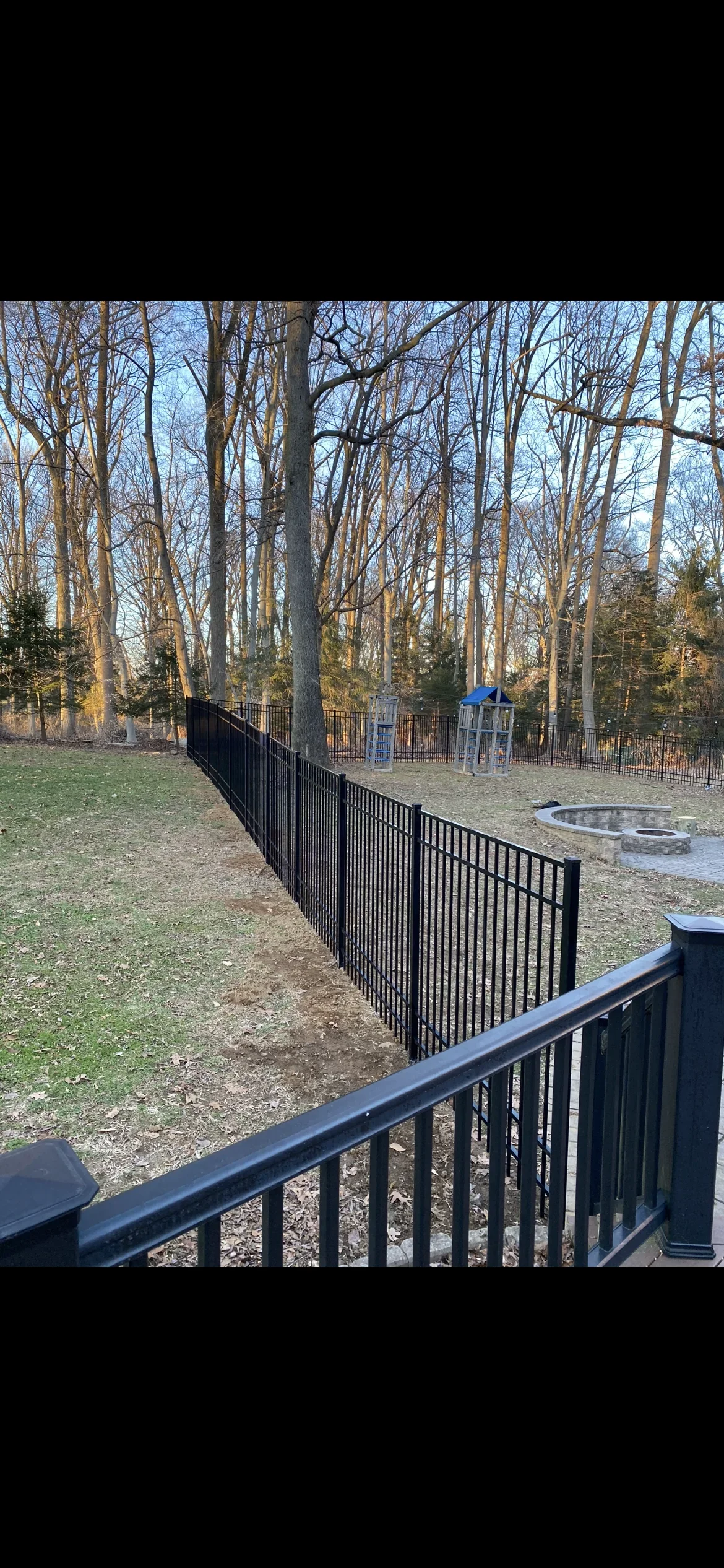 Black aluminum picket fence with horizontal rails installed along wooded property line