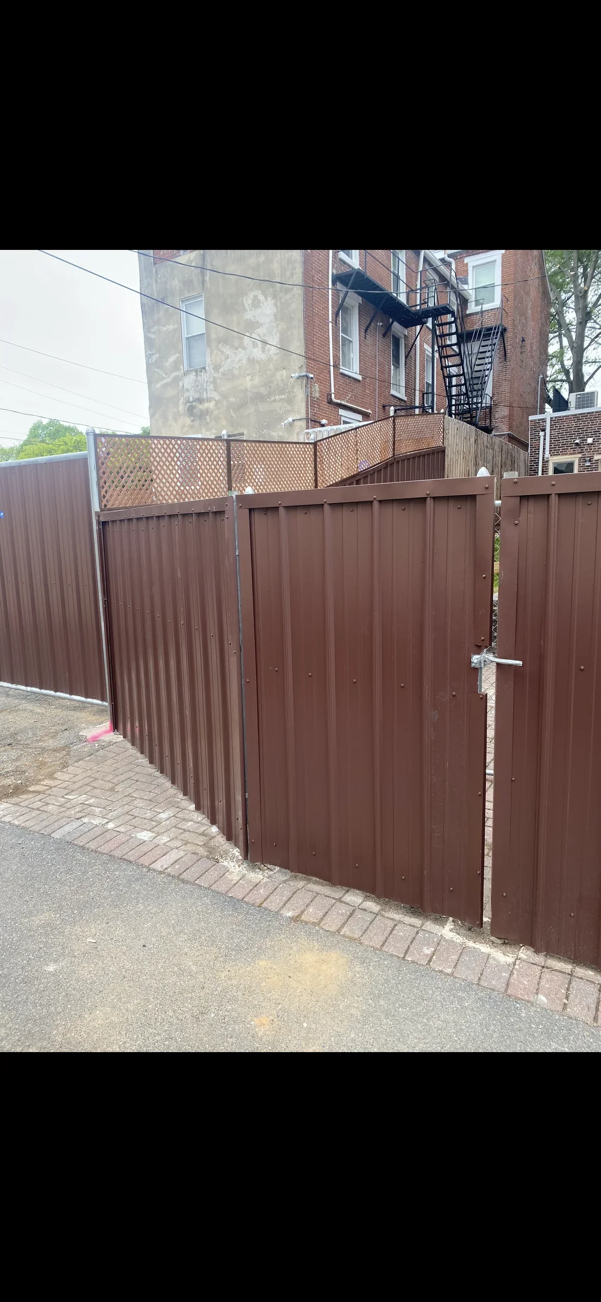 Brown corrugated metal privacy fence with lattice top and matching gate