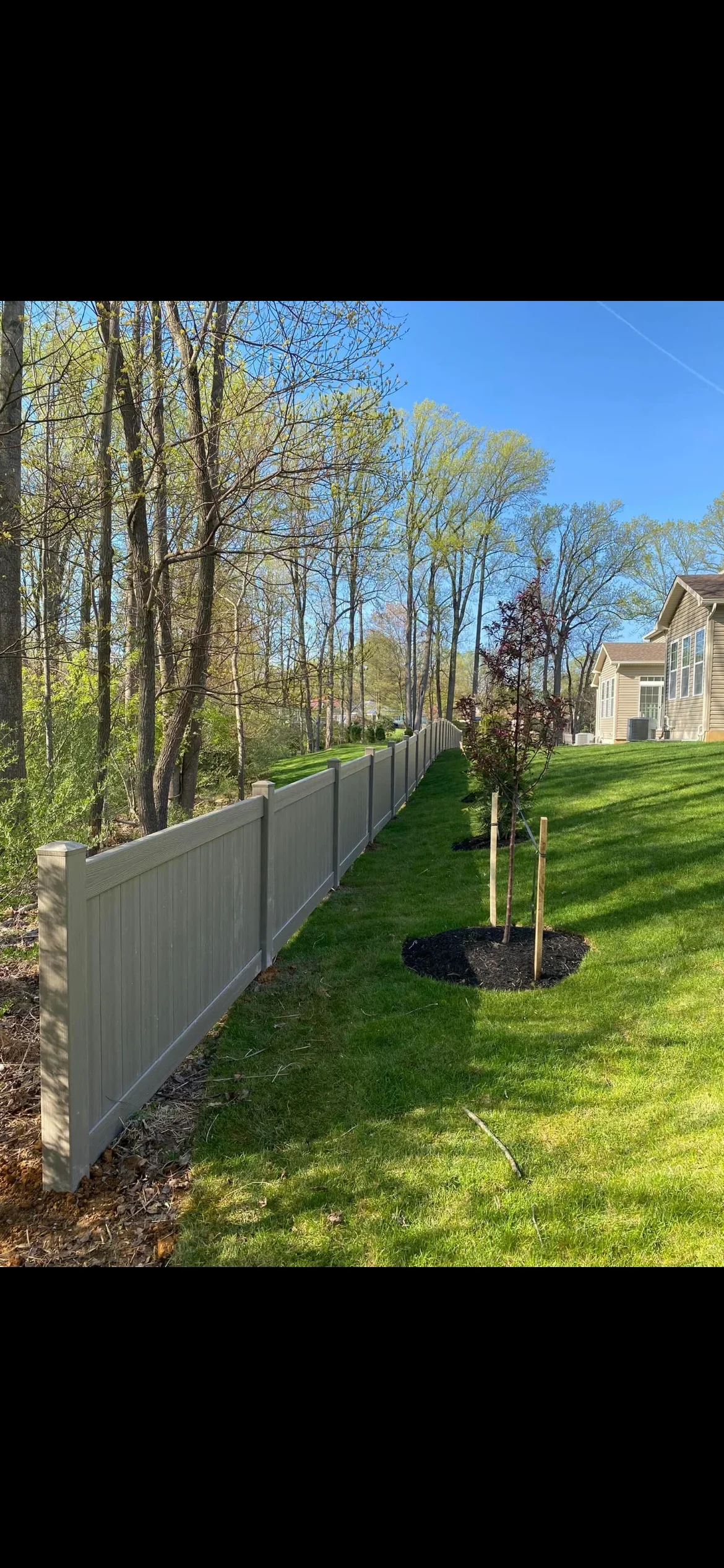 Gray vinyl privacy fence with brick posts installed along property line with trees and lawn