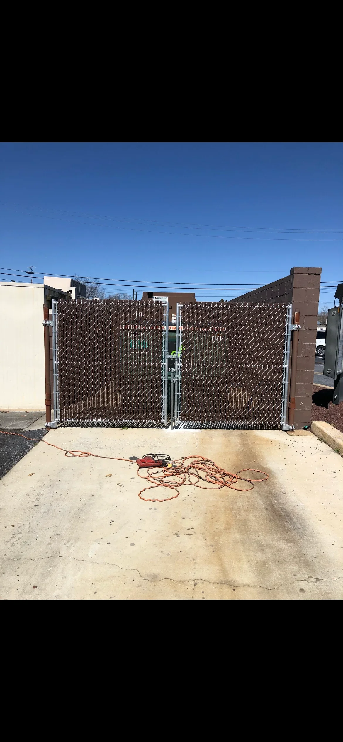 Brown vinyl-coated chain link double gate with aluminum frame and hardware mounted at driveway entrance