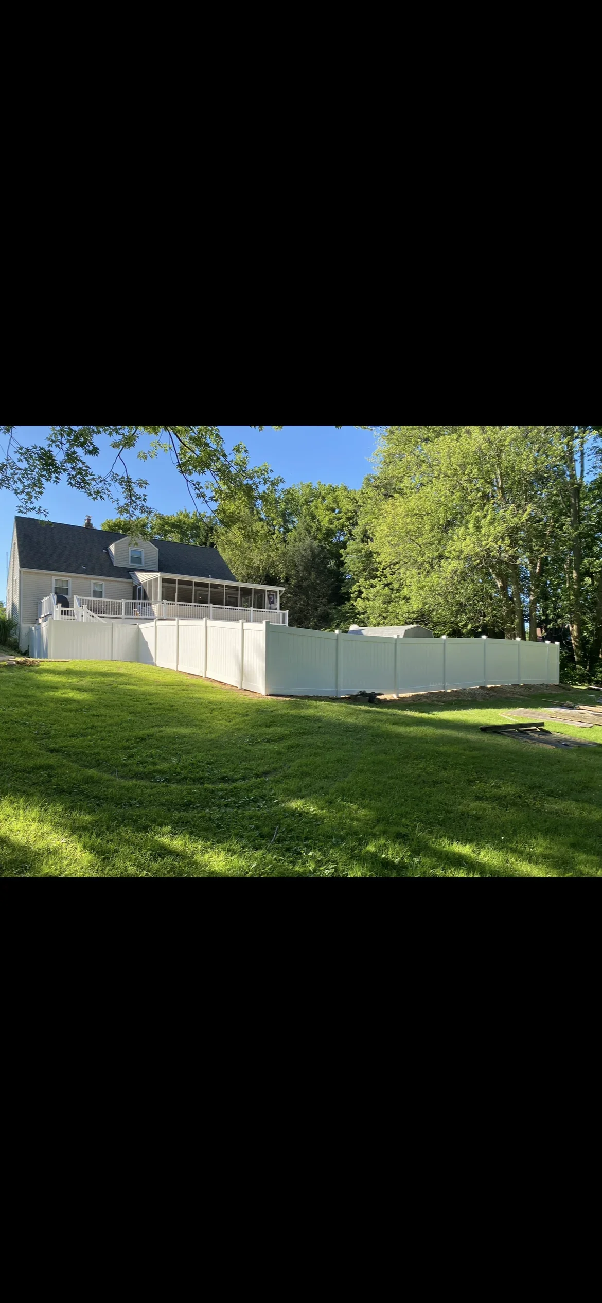 White vinyl privacy fence installed around residential home with green lawn and trees