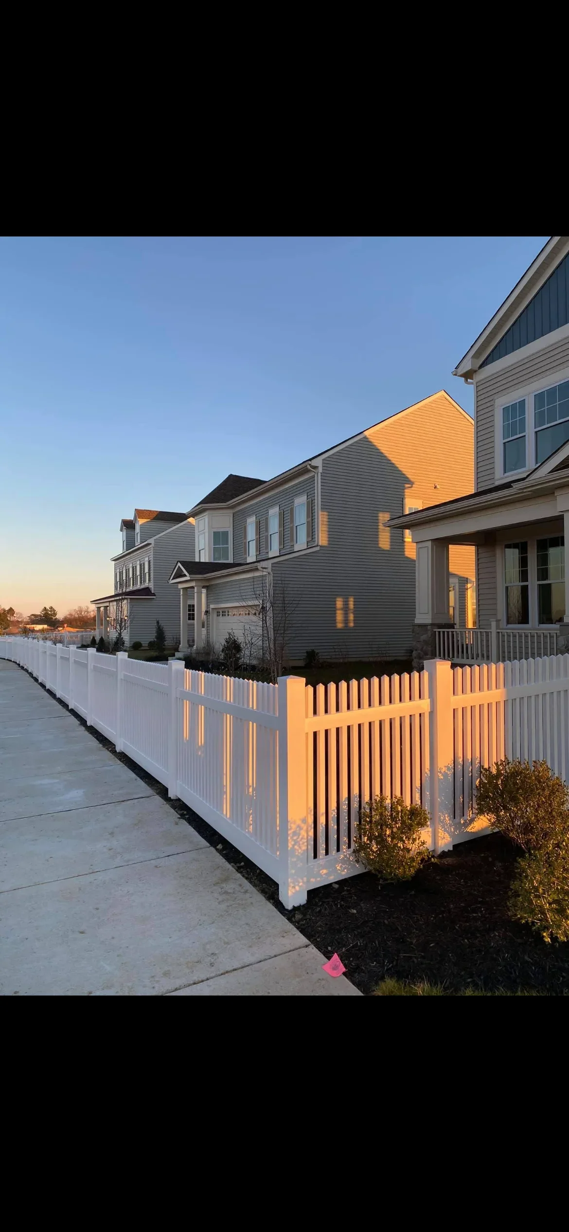 White vinyl picket fence with vertical slats installed along residential driveway